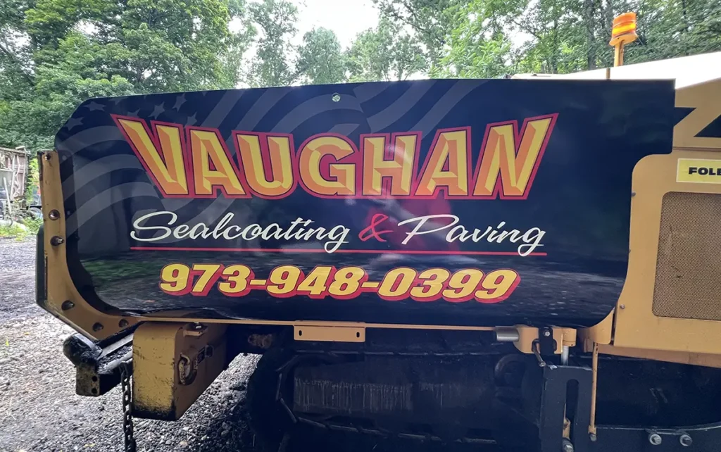 Yellow CAT asphalt paver with black Vaughan Sealcoating & Paving graphics on the side