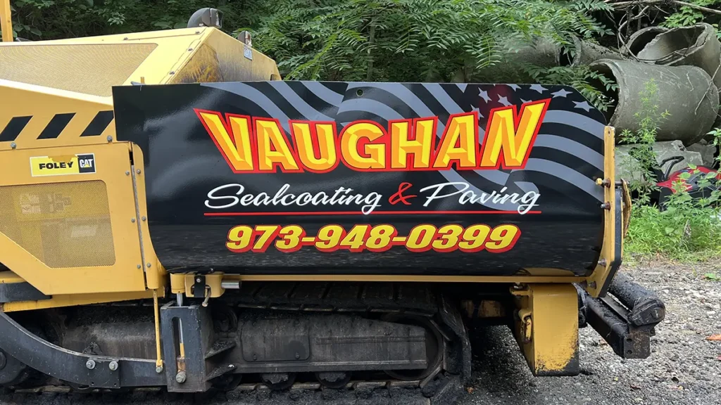 Yellow CAT asphalt paver with black Vaughan Sealcoating & Paving graphics on the side